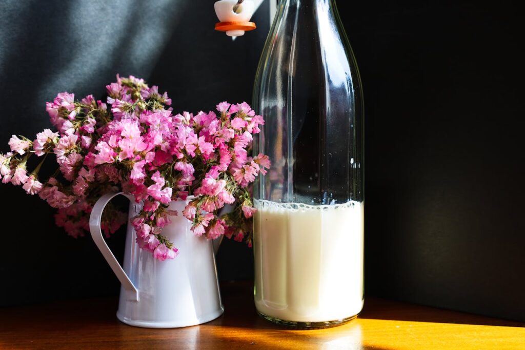 Close-up of pink flowers in a white pitcher beside a glass bottle of milk.