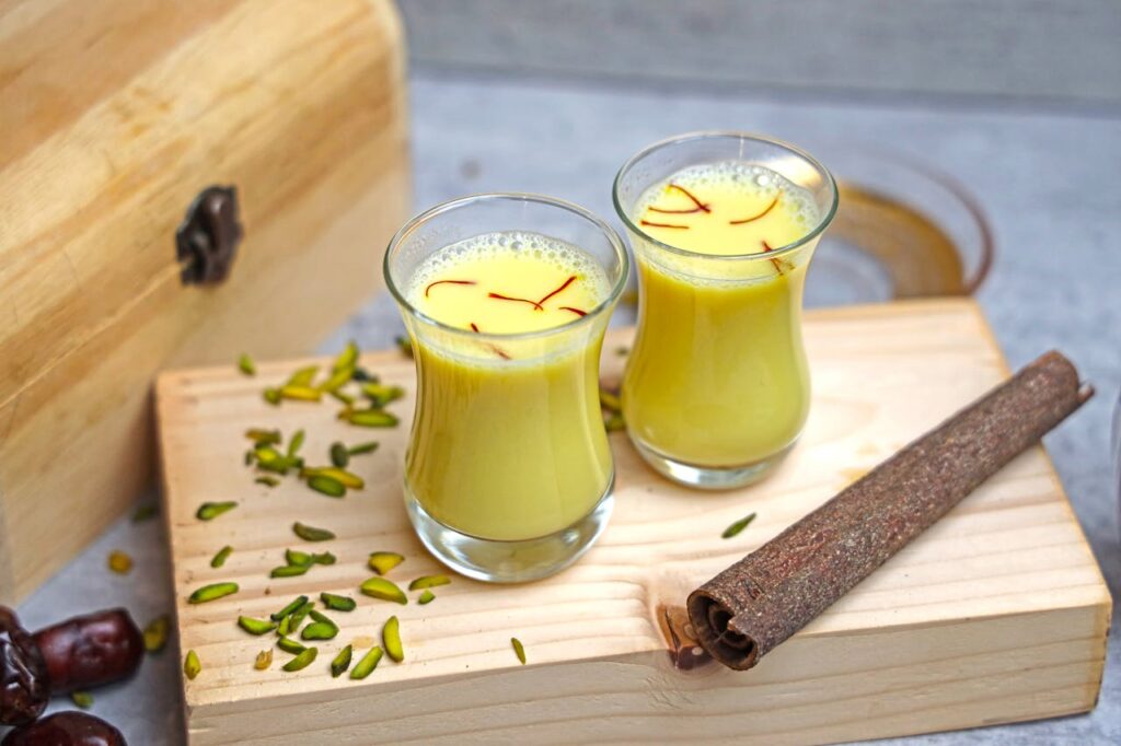 Turmeric and saffron milk on a rustic wooden board, garnished with pistachios.