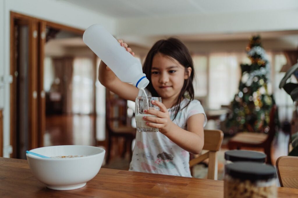 A young girl pouring milk into a glass for breakfast, enjoying a morning meal at home.