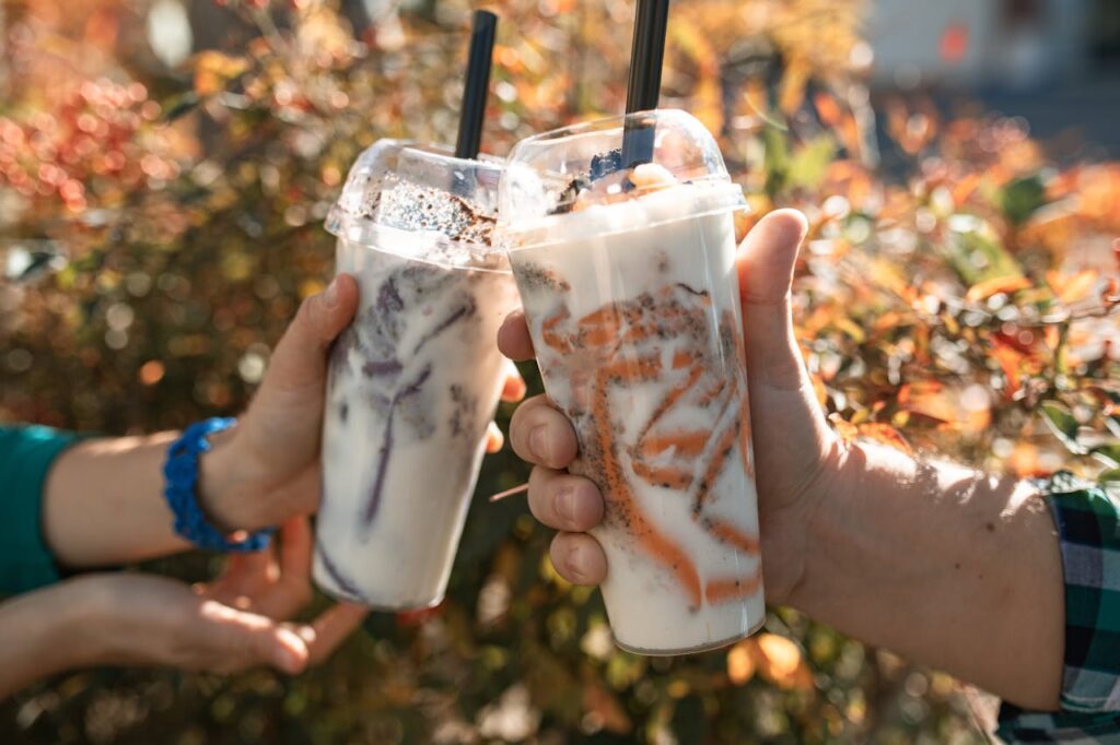 Two people holding colorful bubble teas celebrate outdoors in the warm autumn sun.